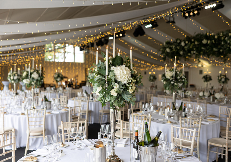 Wedding meal round tables with flower candle centrepieces and fairy light draped ceiling